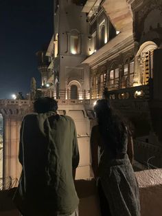 two people standing on the roof of a building at night looking out onto the city