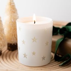 a white candle sitting on top of a wooden table next to two small christmas trees