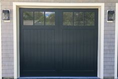 a black garage door in front of a gray house with two lights on each side