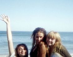 three girls standing on the beach with their arms in the air and one girl holding her hand up