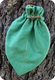 a green bag sitting on the side of a tree trunk with leaves attached to it