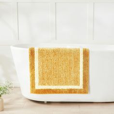 a yellow bath mat sitting on top of a white tub next to a potted plant