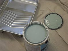 two cans of paint sitting on top of a bed next to a pan with the lid open