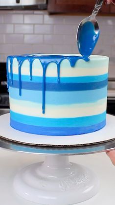 a blue and white striped cake being drizzled with icing