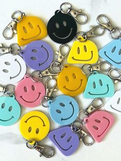 a bunch of smiley face key chains on a white surface with different colors and shapes