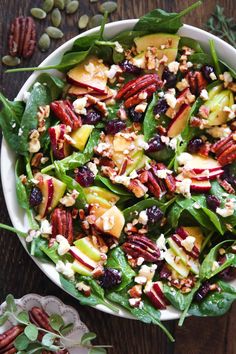 a white bowl filled with spinach salad topped with apples and pecans next to nuts