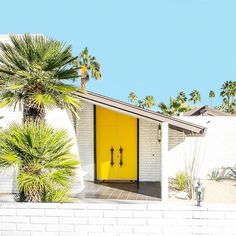 a yellow door sits in front of a white brick house with palm trees around it