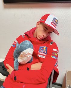 a boy in a red jacket and hat holding a stuffed animal while sitting on a chair