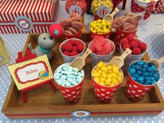 a wooden tray topped with red cups filled with candy next to other cupcakes