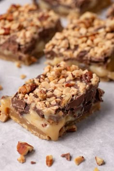 several pieces of dessert sitting on top of a piece of parchment paper covered in nuts