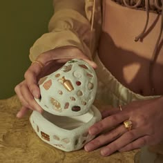 a woman is holding a decorative object in her hands while sitting at a table with other items on it