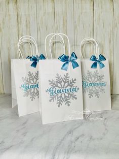 three small white bags with blue bows and snowflakes on them, sitting on a table