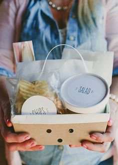 a person holding a box with some food in it and two cups on top of it