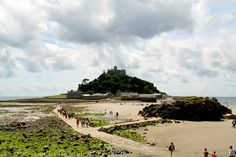 people are walking on the beach near an island with a castle in the background,