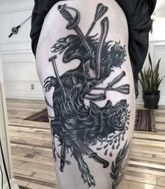 a man's leg with a black and white tattoo design on it, holding two crossed swords