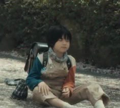 a young boy sitting on the ground with a backpack