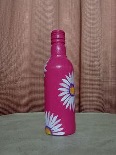 a pink water bottle with white daisies on it sitting on a table next to a curtain