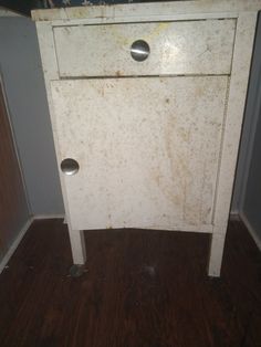 an old white cabinet sitting on top of a wooden floor next to a wall with peeling paint