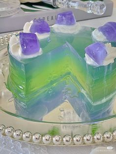 there is a cake with purple and green frosting on the top, sitting on a glass platter