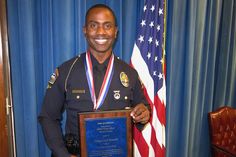 a man in uniform is holding a plaque and smiling at the camera with an american flag behind him