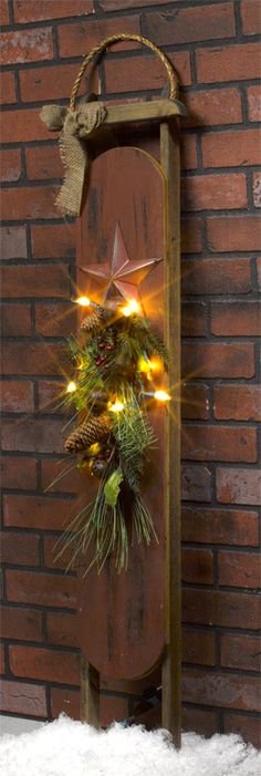 a wooden sled with a wreath and lights hanging from it's side against a brick wall