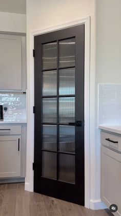 an empty kitchen with white cabinets and black glass front door that leads to the dining room