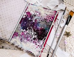 an art journal with paper and paintbrushes laying on top of it, next to crochet doily