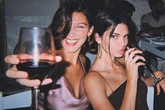 two women sitting at a table with wine glasses in front of them and one holding a cell phone to her ear