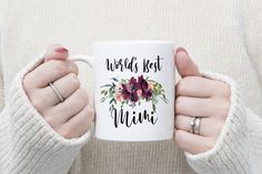 a woman holding a coffee mug that says world's best grandmother with flowers on it