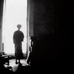 a black and white photo of a person standing in front of a window with the light coming through