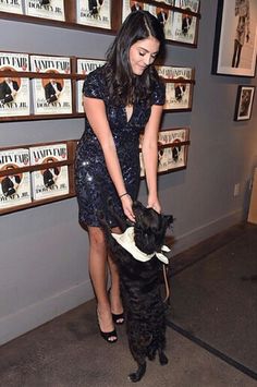 a woman standing next to a black dog on top of a carpeted floor in front of pictures