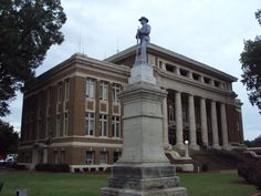 a statue in front of a building with columns on the sides and a man standing on top