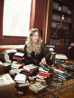 a woman is sitting on the floor surrounded by many books in front of a window