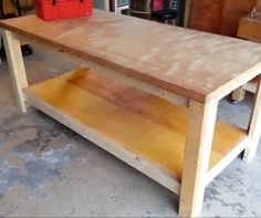 a wooden table sitting in a garage next to a red toolbox on the floor