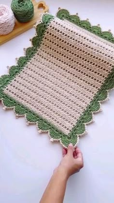 someone is crocheting a green and white afghan on a table next to some yarn