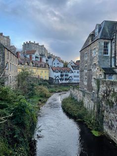 a river running through a small town next to tall buildings on top of a hill