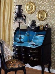 an old fashioned desk and chair in a room with wallpapered walls, gold curtains and black furniture