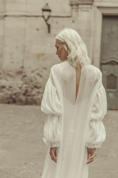 a woman in a white dress is walking down the street with her back to the camera