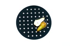 a black plate topped with a pear and an apple on top of cross - stitched circles