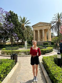 a woman standing in front of a building with trees and bushes around her, looking at the camera