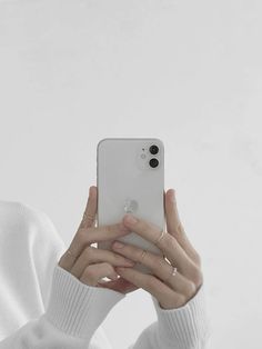 a woman taking a selfie with her cell phone in front of her face while wearing a white sweater