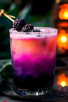 a purple drink with blackberries on the rim and garnished with ice in front of candles