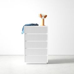 a white cabinet sitting on top of a floor next to a blue towel and an orange vase