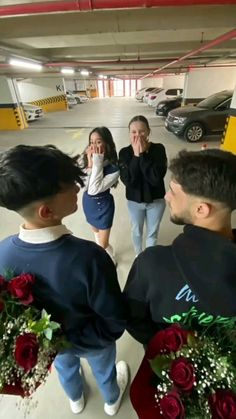 three people standing in a parking garage with flowers on the floor and one person covering his face