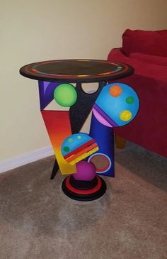 a colorful table and chair in the corner of a room with a red couch behind it