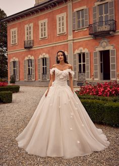 a woman standing in front of a building wearing a wedding dress with flowers on it