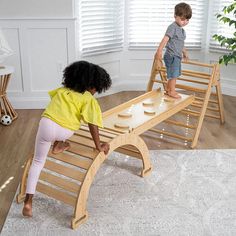 two children playing on a wooden bench in a living room with white walls and hardwood floors