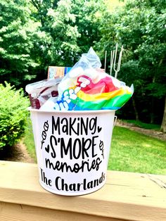 a white bucket filled with candy sitting on top of a wooden deck next to trees