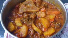 a pot filled with stew and vegetables on top of a tablecloth next to a wooden spoon