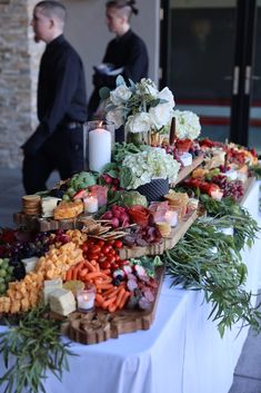 a table topped with lots of different types of fruits and veggies next to two men